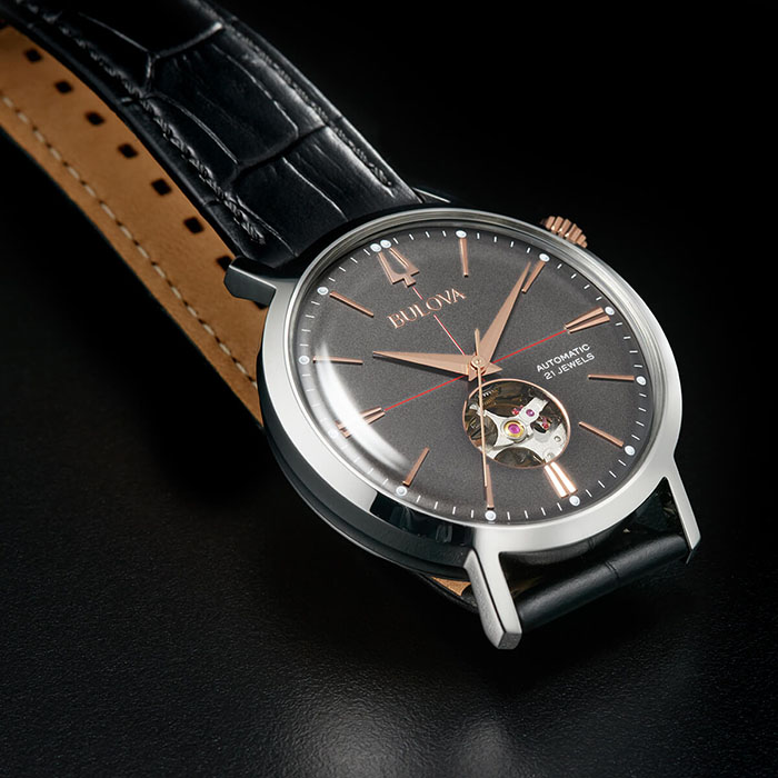 Relógio com pulseira negra de couro e mostrador metálico cinza-escuro da coleção Aerojet de relógios Bulova, inspirada no design vintage típico dos anos 1960.