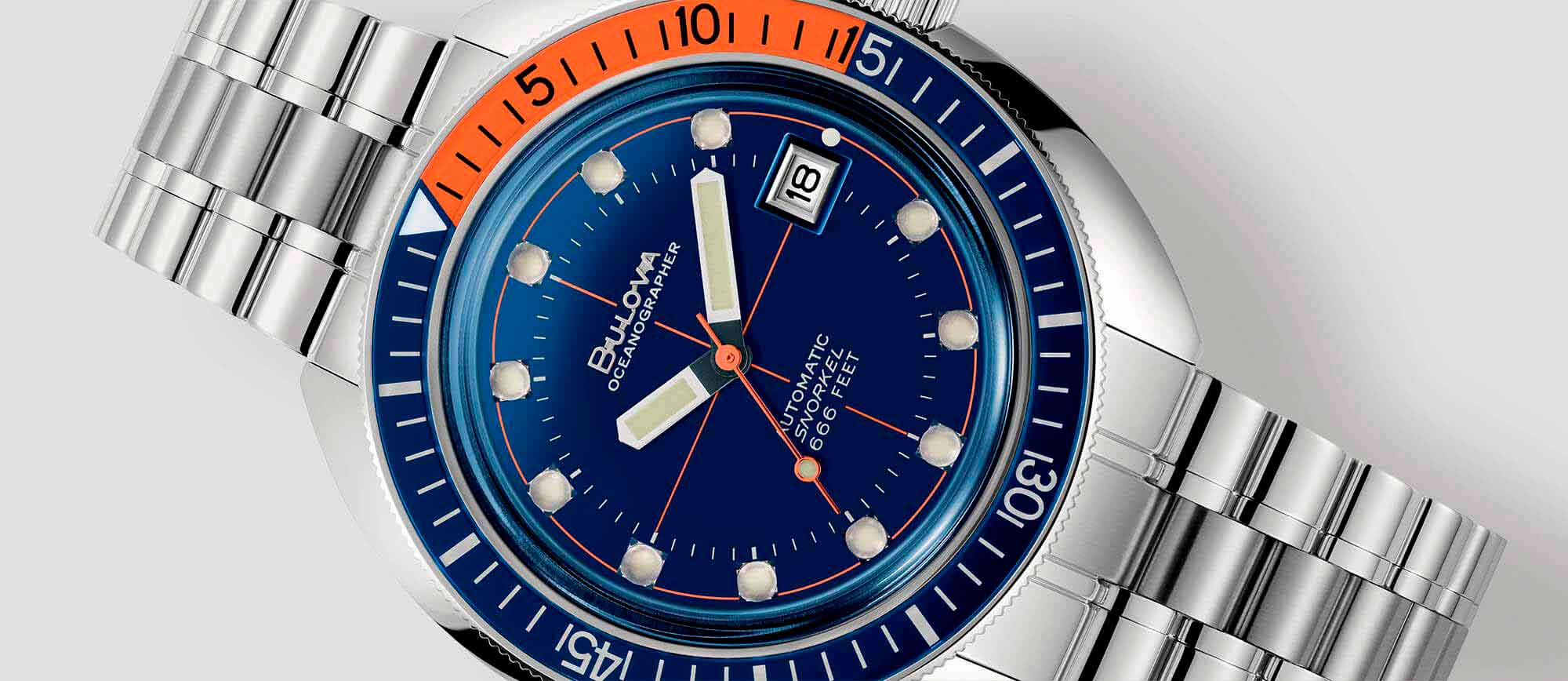 Relógio metálico com mostrador azul, com detalhes em laranja, da coleção Oceanographer "Devil Diver" de relógios Bulova, uma homenagem ao mergulho de profundidade. Relógios resistentes à água.